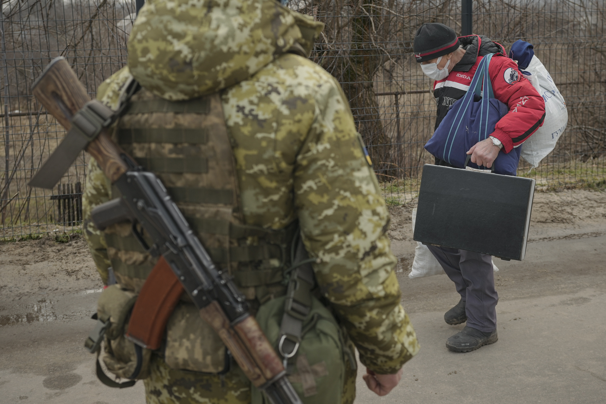 一位老人拿着行李从专业人士面前经过-俄罗斯分离主义者。